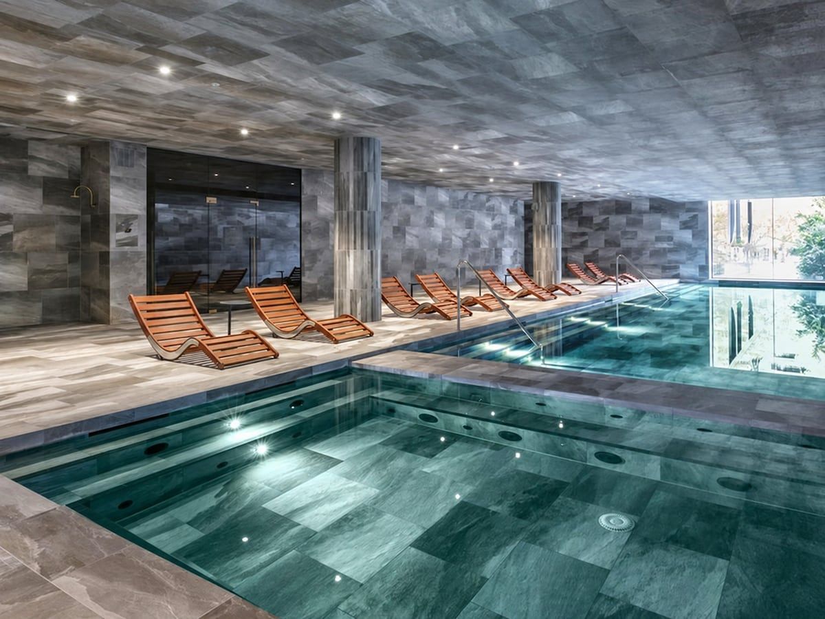 A modern indoor pool area with lounge chairs and a clear pool.