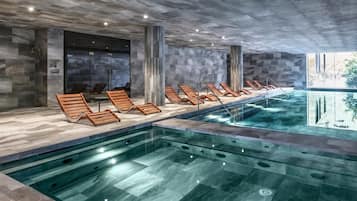 A modern indoor pool area with lounge chairs and a clear pool.