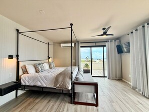 Ein Himmelsbett mit einer Bank, einem Deckenventilator und Blick ins Freie durch große Fenster.
