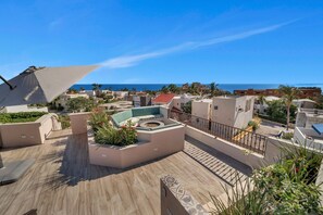 Eine Dachterrasse mit Sitzgelegenheit, Feuerstelle und Blick auf das Meer und die umliegenden Gebäude.
