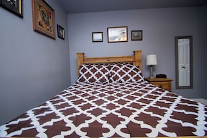 Una cama con una colcha estampada, un cabecero de madera y una mesita de noche con una lámpara.