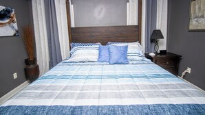 Ein Schlafzimmer mit einem Bett, Vorhängen, einem Nachttisch, einer Lampe und einem Bild an der Wand.