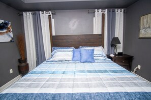 Une chambre à coucher avec un lit, des rideaux, une table de chevet, une lampe et un tableau au mur.