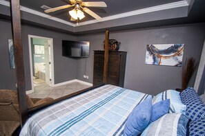 Une chambre à coucher avec un lit, une télévision, un ventilateur de plafond, une commode et un tableau accroché au mur.