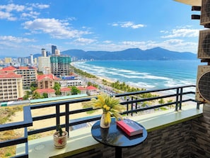 Un balcón con vistas a la playa y al paisaje urbano, una planta en maceta y un libro.
