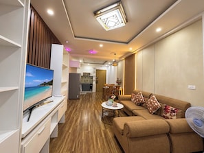 A modern living room with a flat-screen TV, a sofa, a coffee table, and a fan. - My Khe Ocean View Apartment (Đà Nẵng)