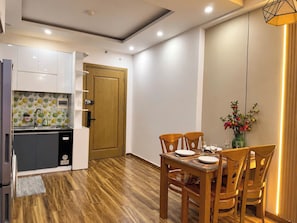 A modern kitchen with a wooden door, a dining table with chairs, and a vase with flowers. - My Khe Ocean View Apartment (Đà Nẵng)