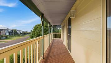 A covered porch with a wooden floor, a railing, and a view of the street and houses in the background.