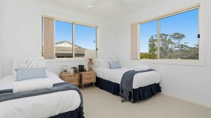 A bedroom with two beds, a nightstand, and a window with a view of trees and a house. - Ebb And Flow near Manyana Beach (Manyana)