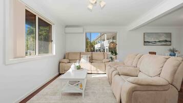 A spacious living room with a large window, a beige sofa, a white coffee table, and a view of a building outside.