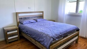 Ein hölzernes Bett mit einem gemusterten Überwurf, zwei Nachttische und ein Fenster mit Vorhängen.
