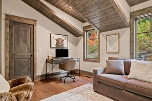 A room with a wooden ceiling, a desk with a computer, a sofa, and a large window with autumn foliage. - Black Diamond  Luxury Unwind: Hot Tub, Game Room, Sleeps 14 (Banner Elk)