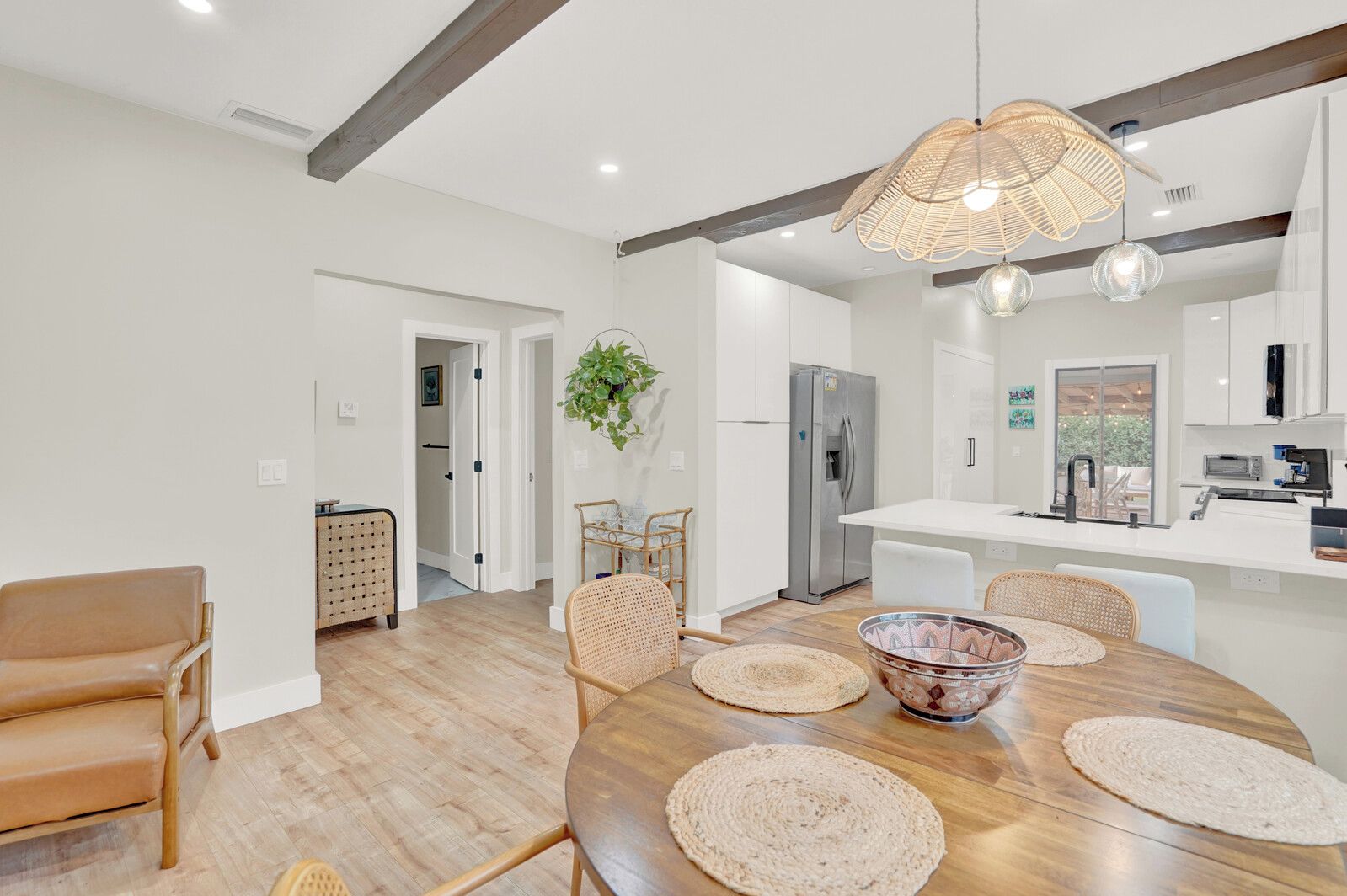 A modern kitchen with white cabinetry, a stainless steel refrigerator, and a dining area with a wooden table and woven placemats.