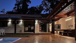A wooden deck with a swimming pool, a covered patio area, and a building with a tiled roof. - Vrbo Property (Moeda)