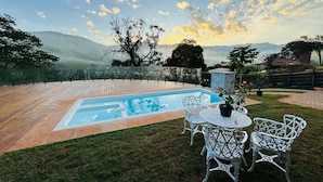 A swimming pool with a view of mountains, surrounded by a grassy area and white metal chairs. - Vrbo Property (Moeda)