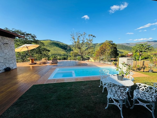 Un patio trasero con piscina, mobiliario exterior y vistas a las colinas.