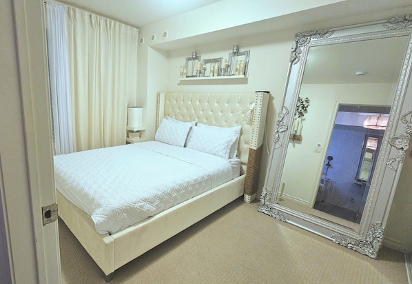 A hotel room with a large bed, a mirror, and a nightstand.