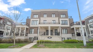 A multi-story residential building with a central entrance, balconies, and a small front yard. - Cozy Nook Near the Lake (Toronto)