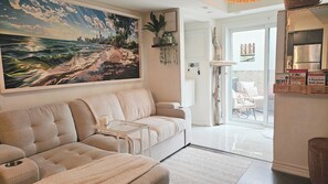 Una sala de estar con un sofá, una mesa de centro de vidrio y un cuadro de una playa.
