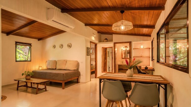 Uma sala aconchegante com sofá, mesa de jantar e cadeiras, e cozinha ao fundo.