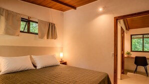 Quarto com cama grande, mesa de cabeceira com abajur, janela com cortinas e porta para outro cômodo.