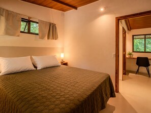 Ein Schlafzimmer mit einem großen Bett, einem Nachttisch mit Lampe, einem Fenster mit Vorhängen und einer Tür zu einem anderen Raum.
