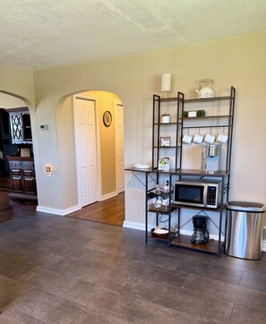 A kitchen area with a coffee station, microwave, and a trash can.