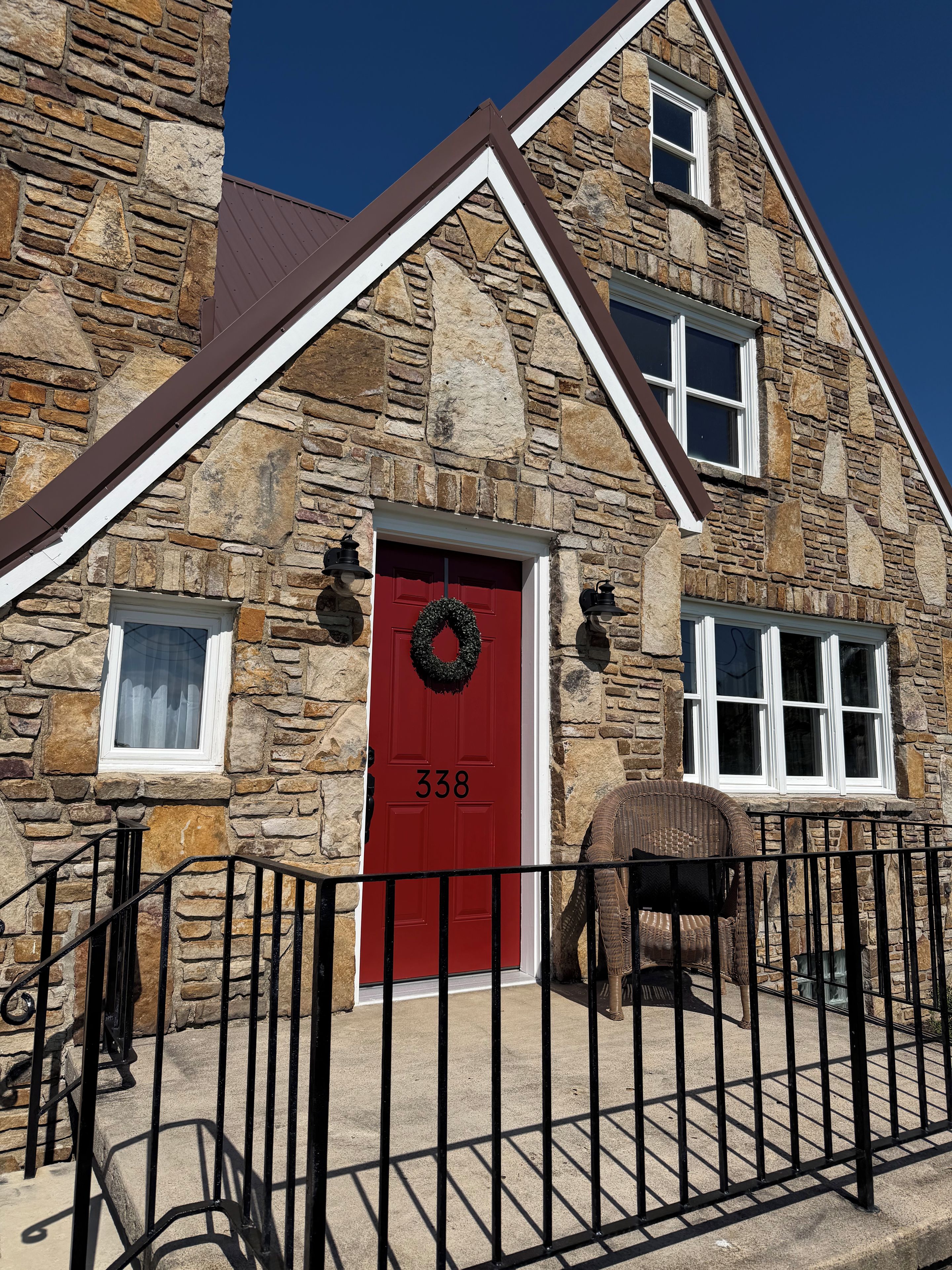 Un bâtiment en pierre avec une porte rouge, portant le numéro 338, et une clôture en métal noir à l’avant.