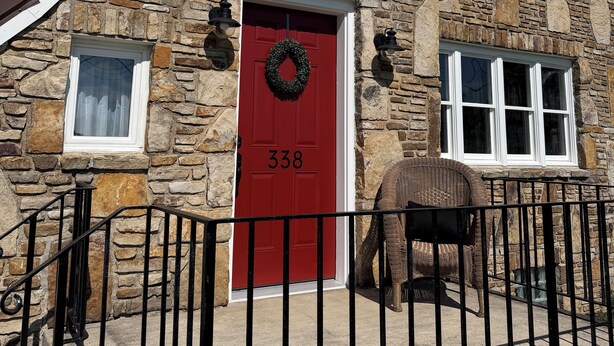Edifício de pedra com porta vermelha, numerado 338, e cerca de metal preta na frente.