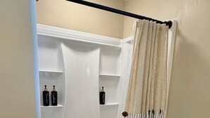Um chuveiro sem barreiras com interior branco, uma cortina bege e duas garrafas nas prateleiras.
