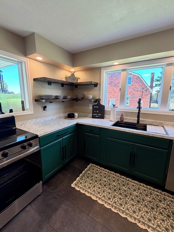 A kitchen with teal cabinets, a black stove, and a window with a view of a brick building.