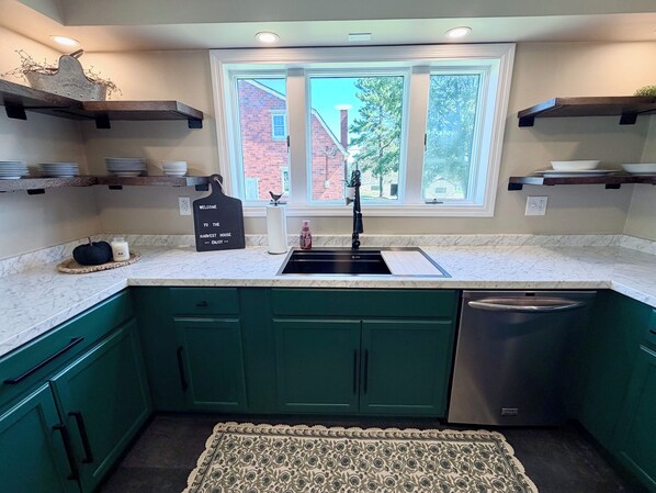 A kitchen with green cabinets, a sink, and a window with a view of a brick house.