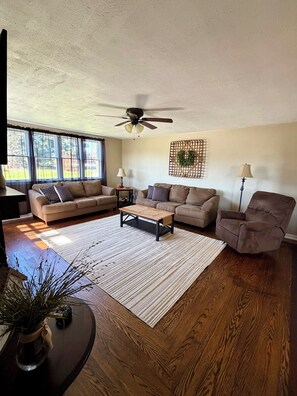 A living room with a ceiling fan, two couches, a coffee table, a side table with lamps, and a floor lamp.