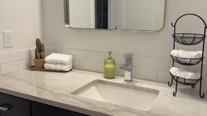 Een badkamer met een wit wastafelmeubel, een spiegel, een waterkraan, een zeepdispenser en een handdoekhouder.