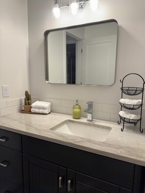 Une salle de bain avec un lavabo blanc, un miroir, un robinet, un distributeur de savon et un porte-serviettes.