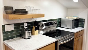 Een moderne keuken met houten kastjes, een roestvrijstalen fornuis en een magnetron. Er zijn planken met servies en een plant.