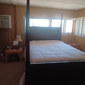 Ein Zimmer mit einem Himmelbett, einem Nachttisch mit Lampe, einem Radio und einem kleinen Tisch mit einem Korb.