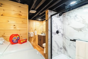 Ein modernes Badezimmer mit einer Holzwand, einer Marmerdusche und einem weißen Waschbecken.