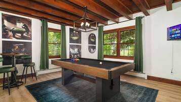 A pool table in a room with large windows, a ceiling fan, and a mounted TV.