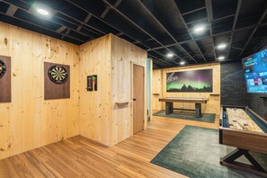A room with wooden walls, a dartboard, a foosball table, and a TV screen displaying a sale.
