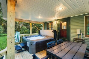 Ein Whirlpool auf einer Holzterrasse mit Tisch und Stühlen, umgeben von einer überdachten Veranda mit Blick auf den Wald.