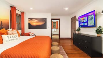 Ein Schlafzimmer mit einem großen Bett, einem an der Wand befestigten Fernseher und Blick ins Freie durch ein Fenster.