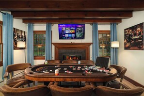 A room with a poker table, chairs, a fireplace, a television displaying a streaming service, and framed artwork on the walls.