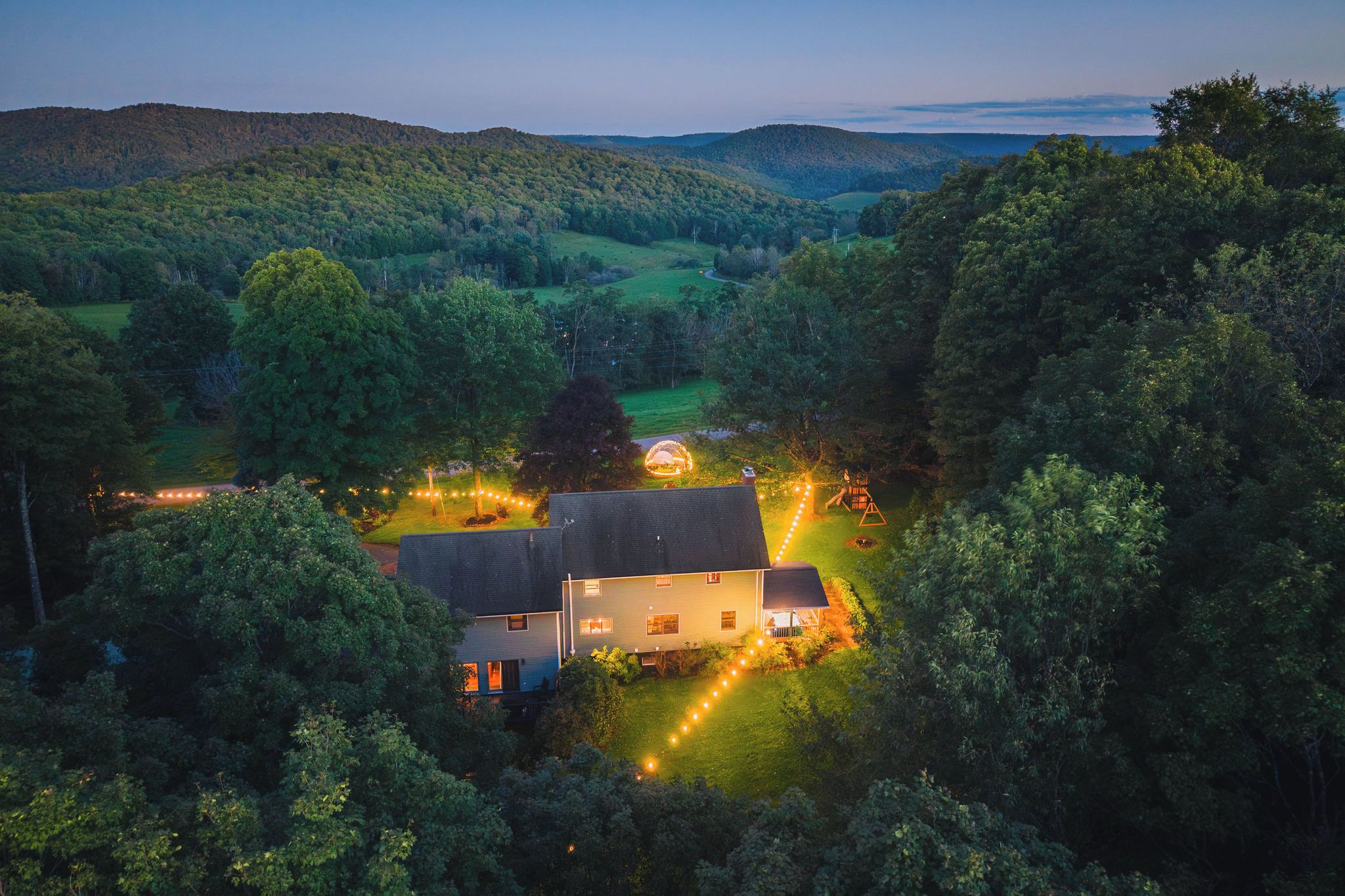 Une maison entourée d’arbres, avec vue sur des collines au loin.