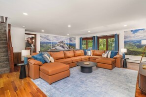 Uma sala de estar moderna com um sofá modular, uma mesa de centro e vista para uma paisagem montanhosa através de grandes janelas.