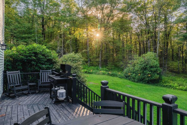 A deck with outdoor furniture and a grill, surrounded by a forested area.
