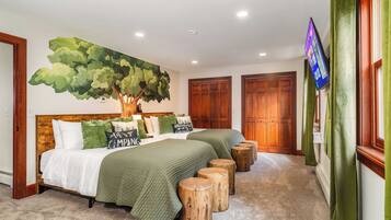 A bedroom with a large bed, two bedside tables, a wall-mounted TV, and a large tree mural.