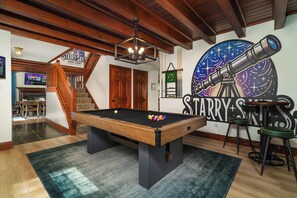 A pool table with a billiards cue ball, a billiards rack, and a wall mural with a telescope.