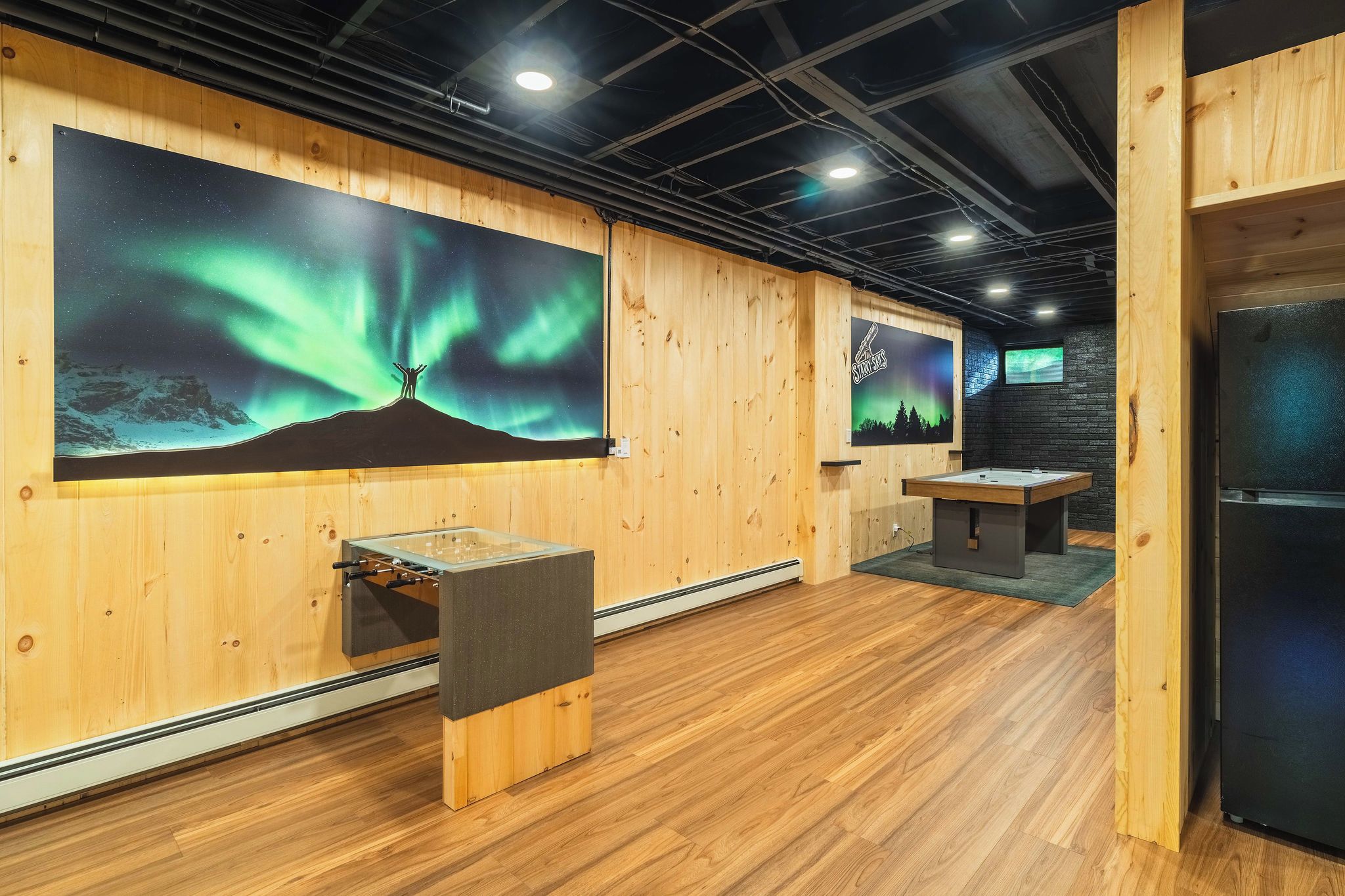A room with wooden walls, a large wall-mounted screen displaying the Northern Lights, a foosball table, and a door.