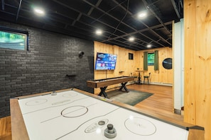 Una habitación con mesa de futbolín, televisor montado en una pared de ladrillo y paneles de madera.